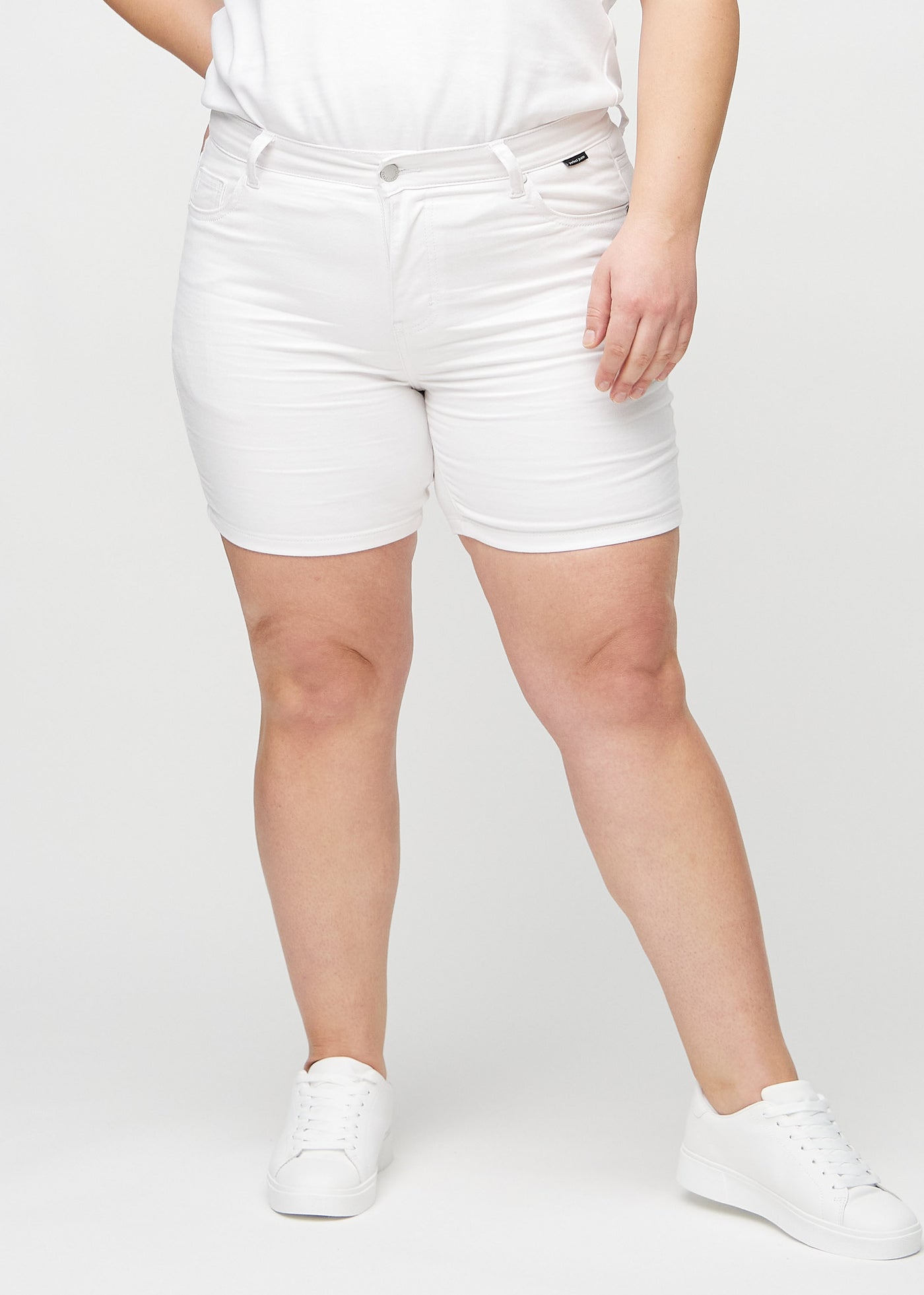 Hvide skinny short shorts, modelnavn Marguerites, som sidder tæt til, og slutter midt på låret på en plus-size model, set forfra.