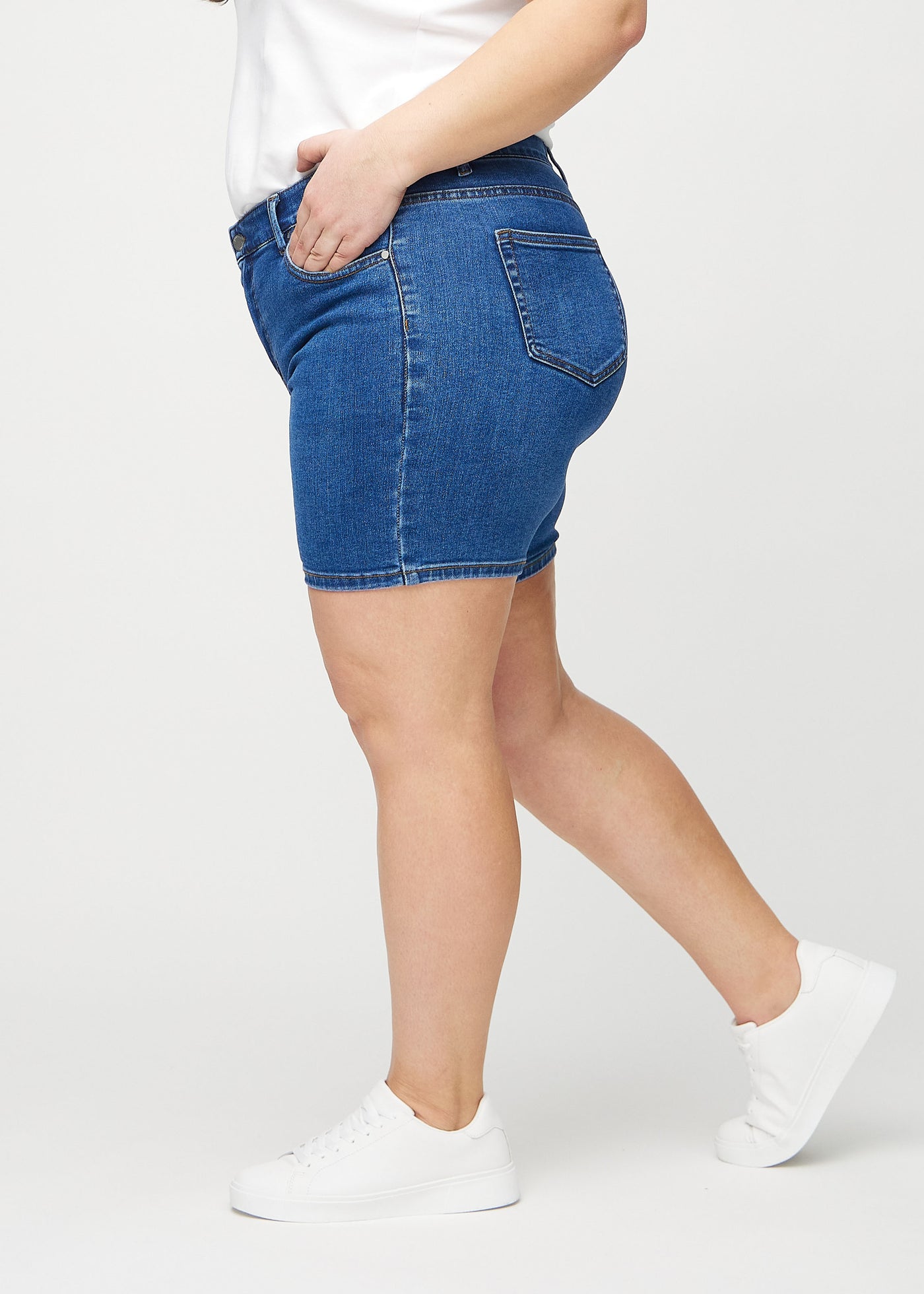 Mørk denim skinny short shorts set fra siden på en plus-size model.