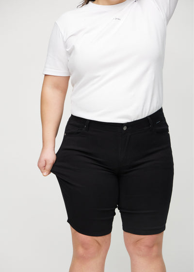 Plus-size model strækker shortsene ved låret for at vise stretch.