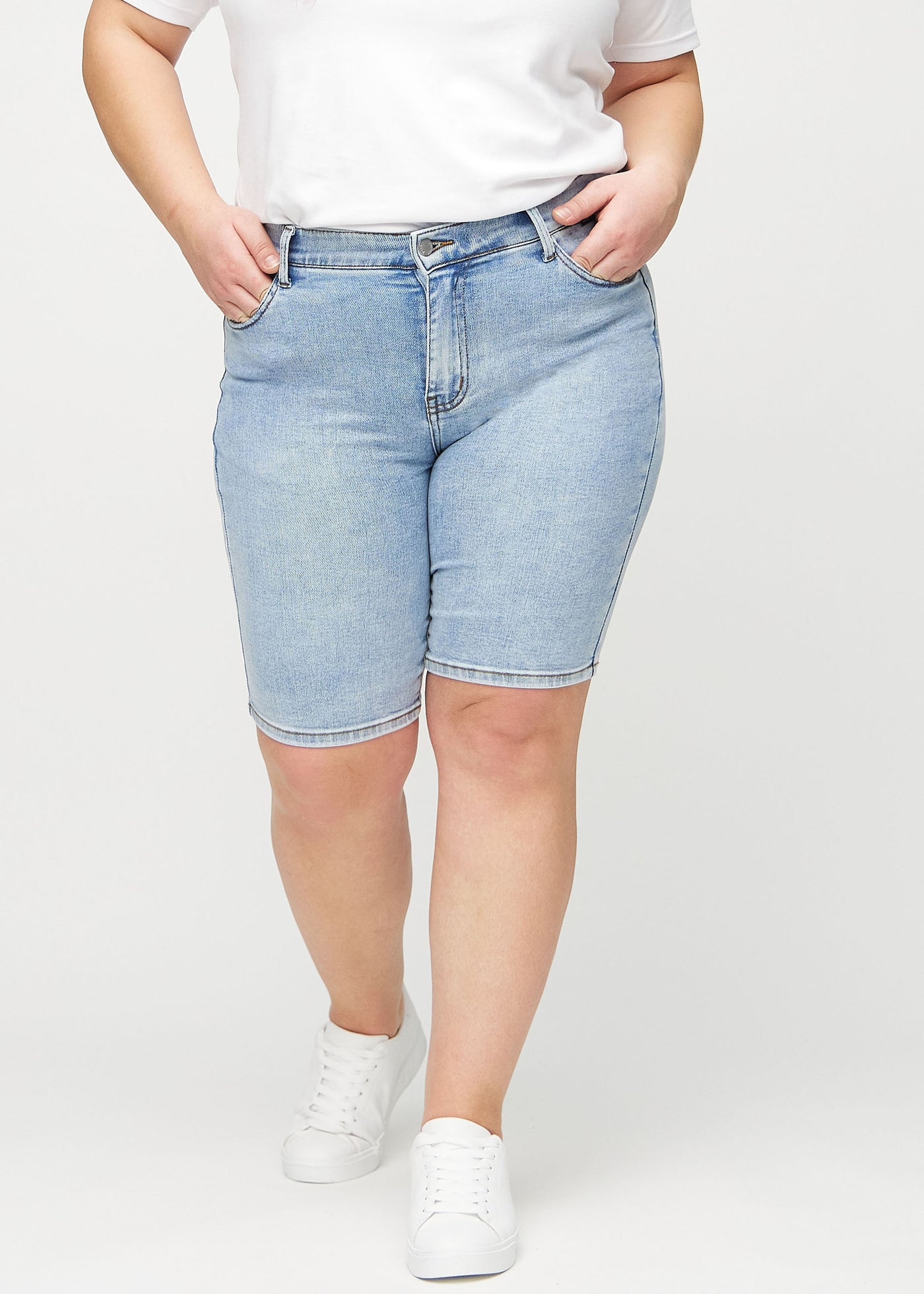 Lys denim skinny middle shorts, modelnavn Waves, som sidder tæt til låret og slutter lige over knæet på en plus-size model, set forfra.