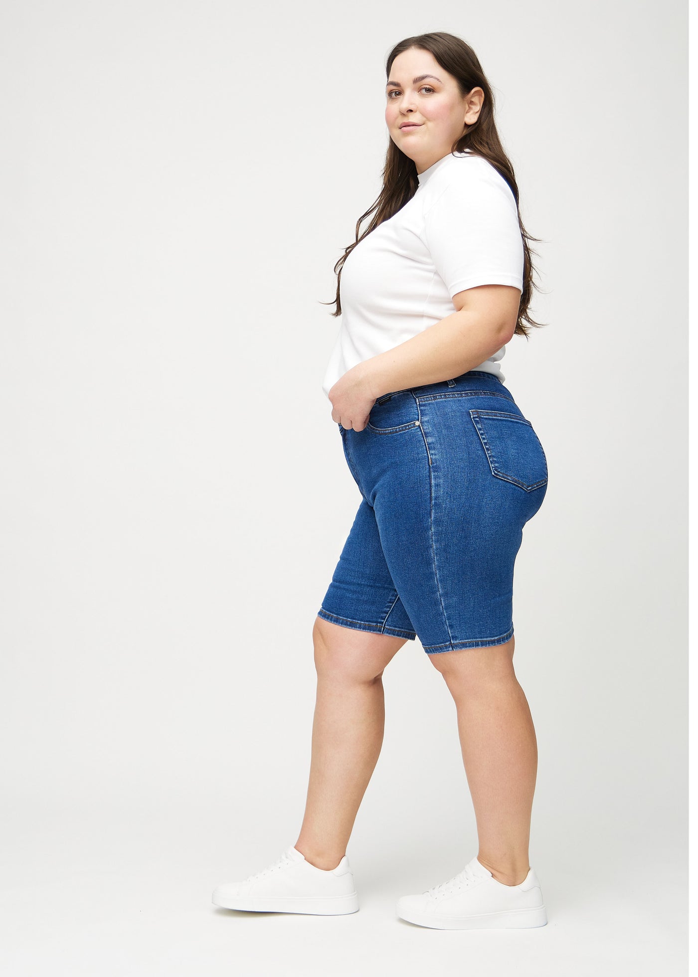 Mørk denim skinny middle shorts set fra siden på en plus-size model.