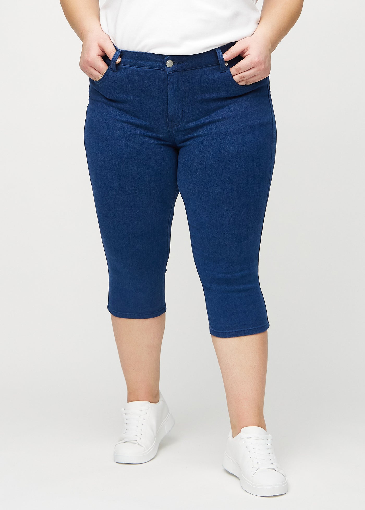 Mørkeblå skinny capris, modelnavn Royals, som sidder tæt til benet og slutter lige under knæet på en plus-size model, set forfra.