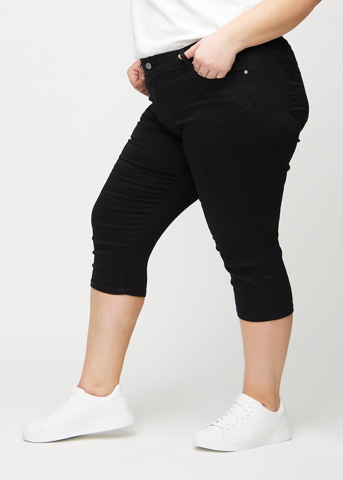 Sorte skinny capris set fra siden på en plus-size model.