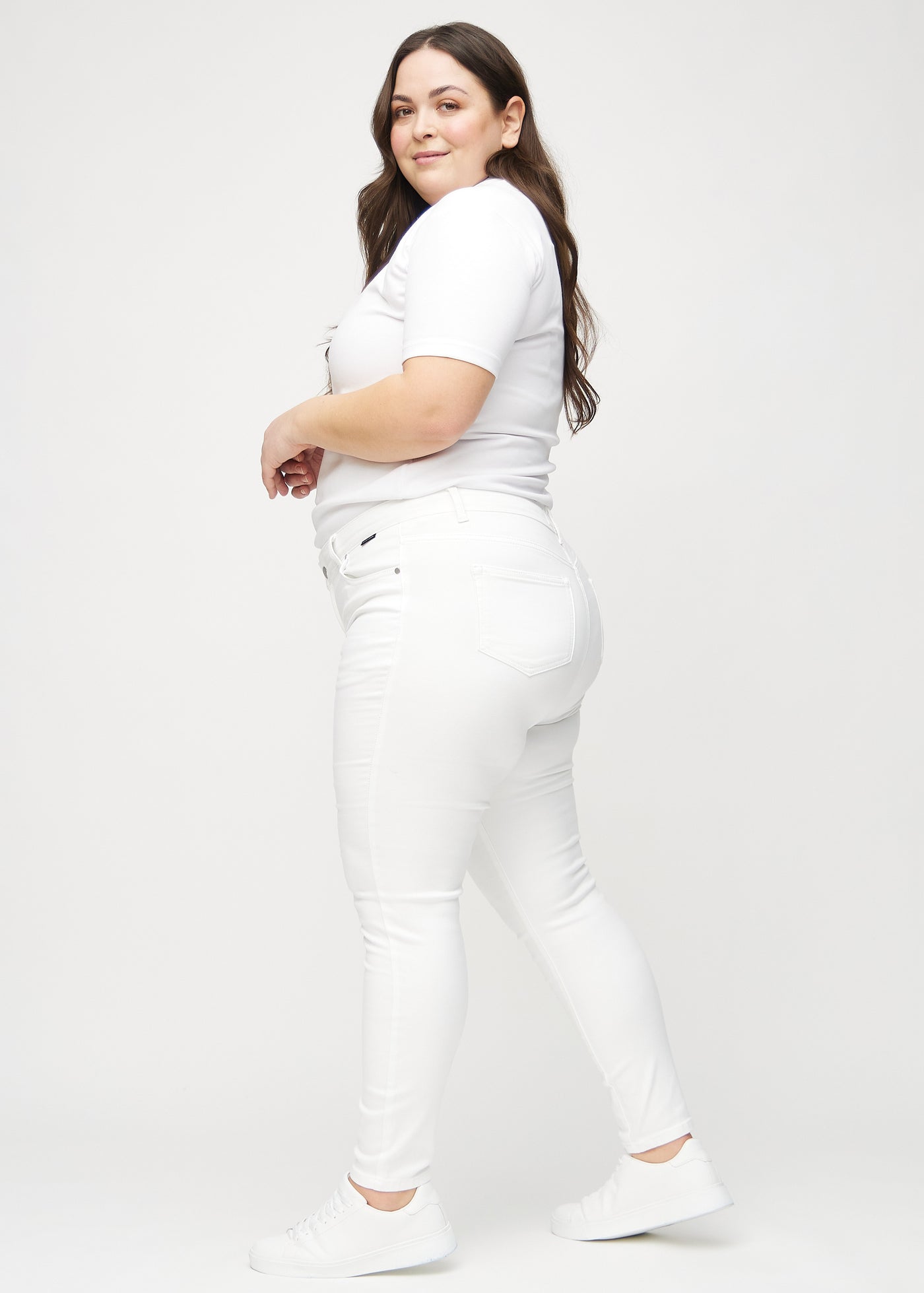 Hvide skinny jeans set fra siden på en plus-size model.