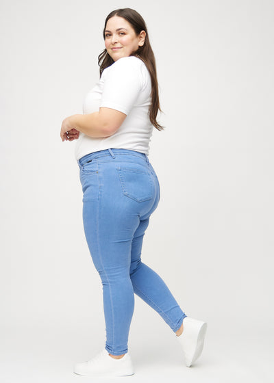 Blå skinny jeans set fra siden på en plus-size model.