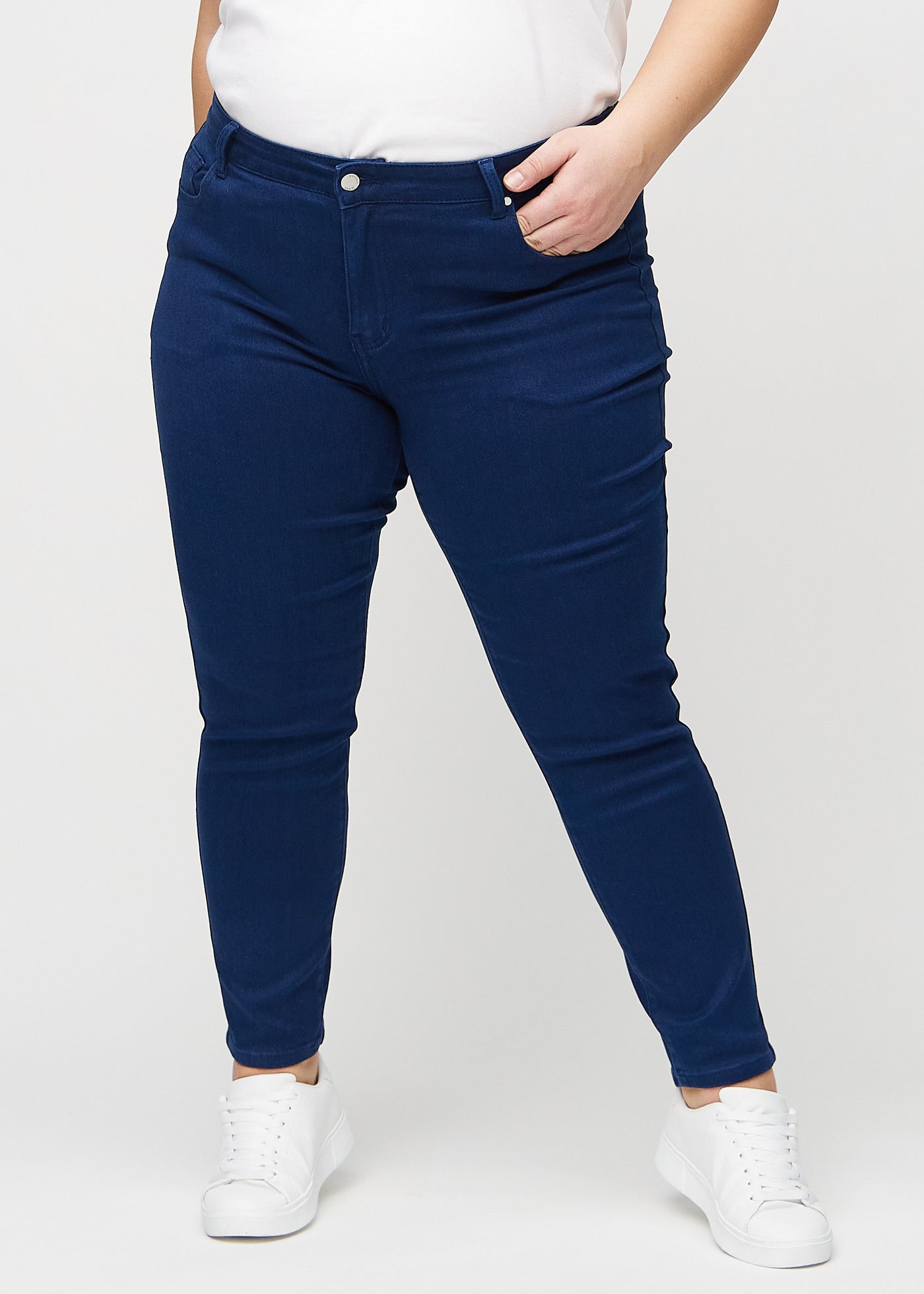 Mørkeblå slim jeans, modelnavn Royals, som sidder tæt til benet, dog lidt løsere ved anklen, på en plus-size model, set forfra.